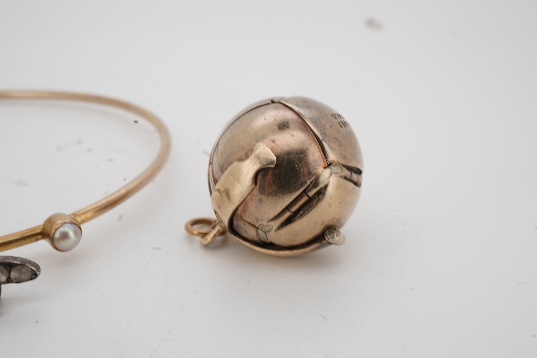 A Masonic ball pendant and a pearl and diamond bangle, early 20th century, the Masonic ball folding open to reveal a cross shape engraved with Masonic symbols, in gilt silver, length 2.2cm when closed, stamped Silver & G